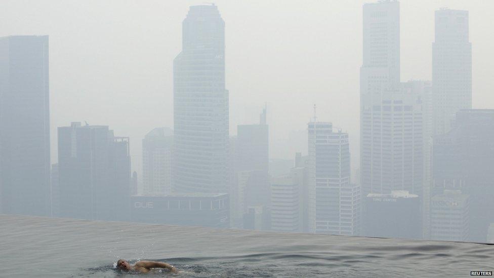 A hotel guest swims in the pool of the Marina Bay Sands Skypark overlooking the haze covered skyline of Singapore 17 June 2013