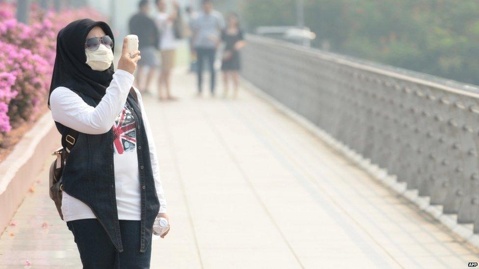 A woman wearing a face mask uses a mobile phone as Singapore suffered a second day blanketed in a thick haze on 18 June 2013