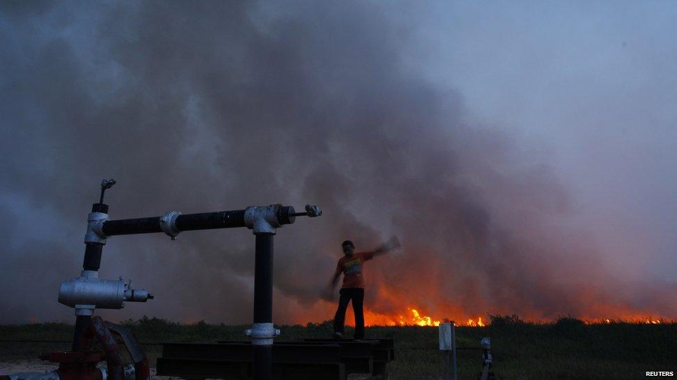 A villager stands on an oil well as fire burns a palm-oil plantation in haze-hit Bangko Pusako district in Rokan Hilir, Indonesia's Riau province, June 22