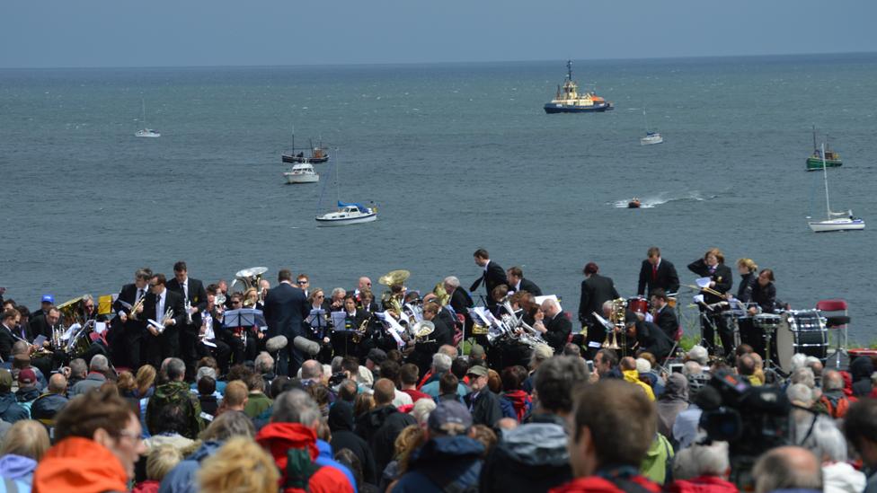 Brass band, crowds and vessels taking part in Foghorn Requiem