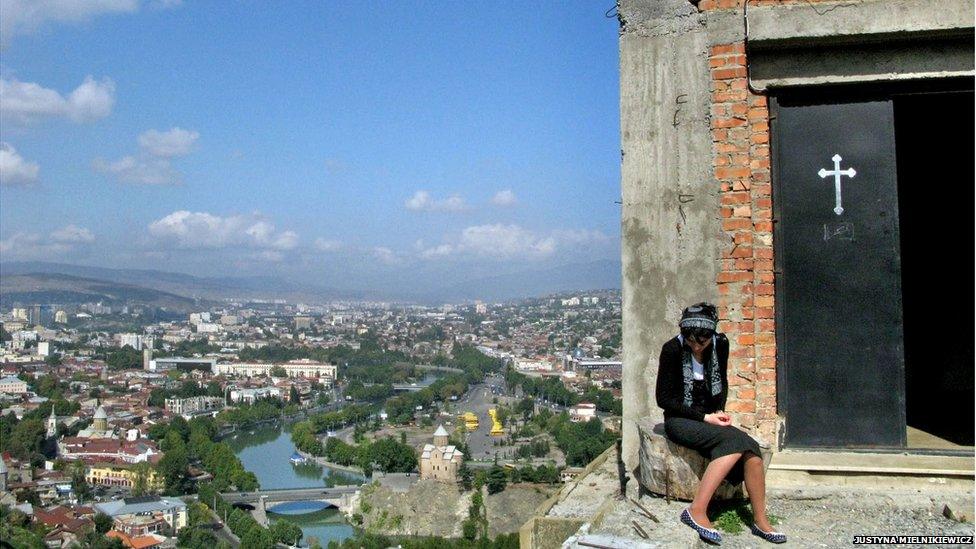 A woman seated outside a church door on heights over looking Tbilisi, Georgia