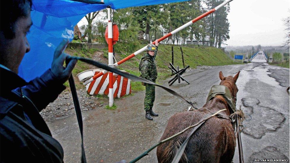 A soldier at a check point raises a barrier to let a man driving a horse and cart pass.