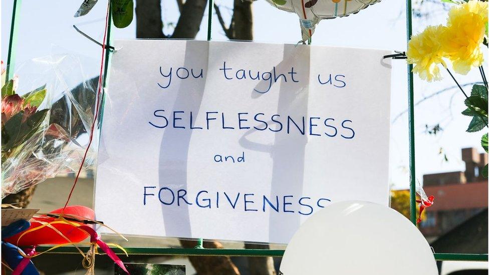 A handwritten poster against railings outside the hospital reads: "You taught us selflessness and forgiveness"