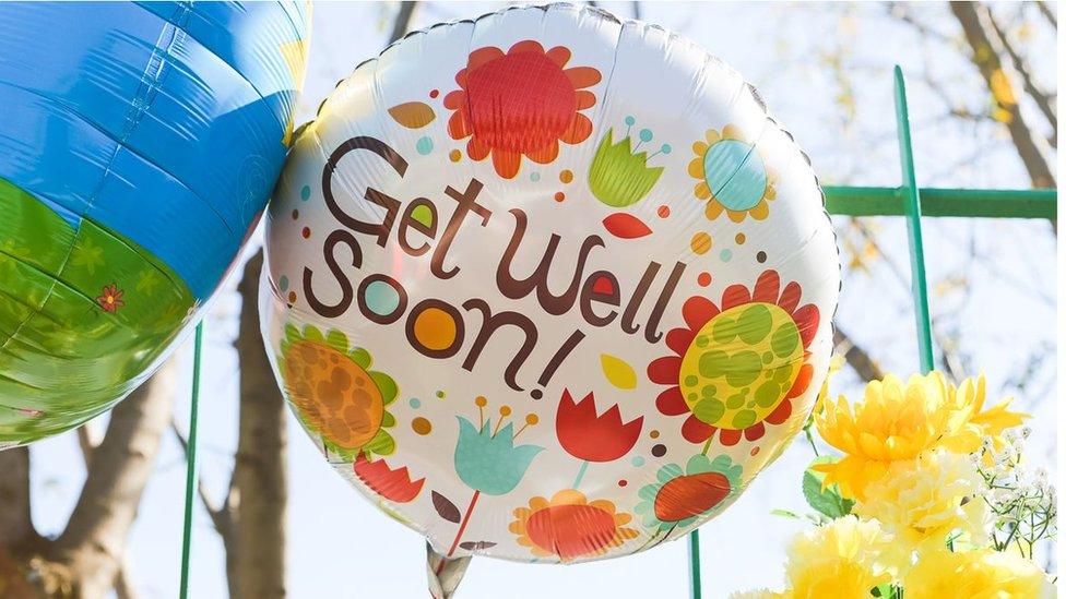 A mass-produced balloon against the railings bears the message: "Get well soon!"