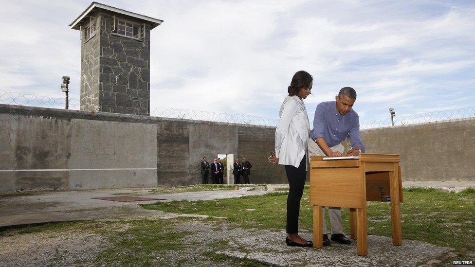 President Obama writes in a guest book as he tours Robben Island with First Lady Michelle