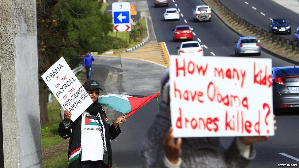 Protesters wave placards outside the University of Cape Town in advance of President Obama's speech there