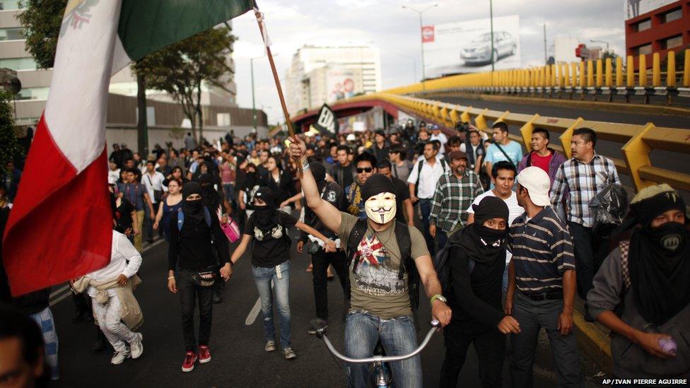 A masked demonstrator holds up a Mexican flag during a march to protest against an alleged government plan to privatize Pemex, 1 July