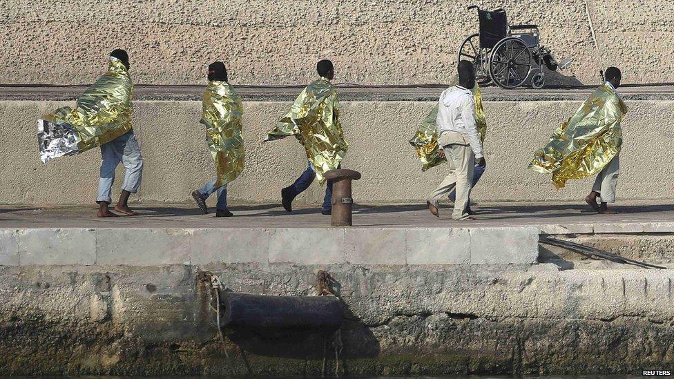 Migrants walk along dock in Lampedusa