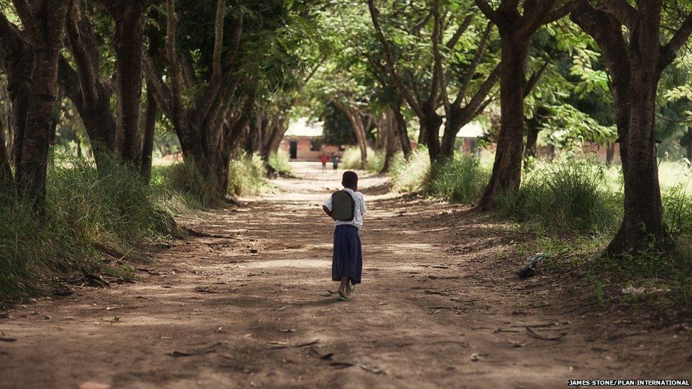Tanzanian schoolgirl Sylvia walking down a tree-lined avenue to her school