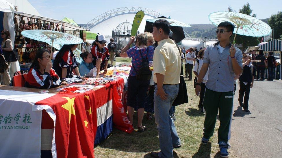 Visitors and competitors use umbrellas to get out of the sun