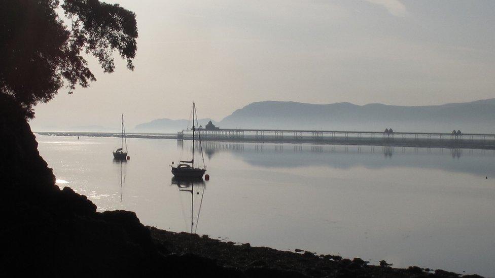 Bangor Pier from the shore of the Menai Strait early on a quiet summer morning. Taken by John Smith of Glyn Garth, Anglesey, from the bottom of the public footpath by Plas Rhianfa.