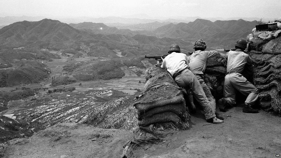 Three South Korean riflemen man a position in the hills as they watch movement of Communist troops in the area beneath them.