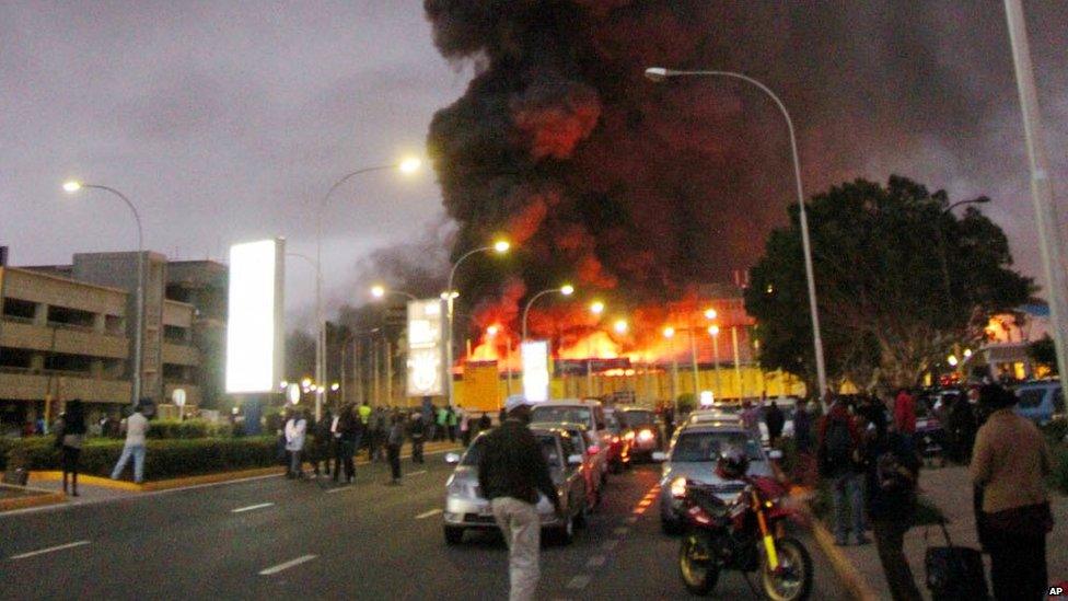 People watch dense black smoke billowing from the Jomo Kenyatta International Airport in Nairobi, Kenya, early Wednesday 7 Aug 2013.