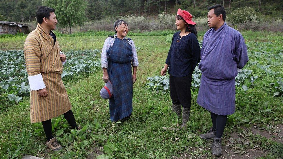 Bhutanese men in traditional robes visiting farm workers Tashi Dema and Tshering Pelden.