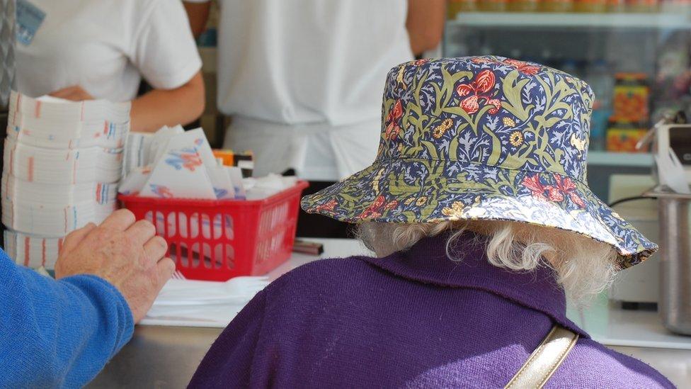 "Gymrwch chi halen a finegr?" Gwraig mewn het patrwm William Morris yn prynu pysgod a sglodion / "Salt and vinegar?" A lady in a William Morris hat buying fish and chips