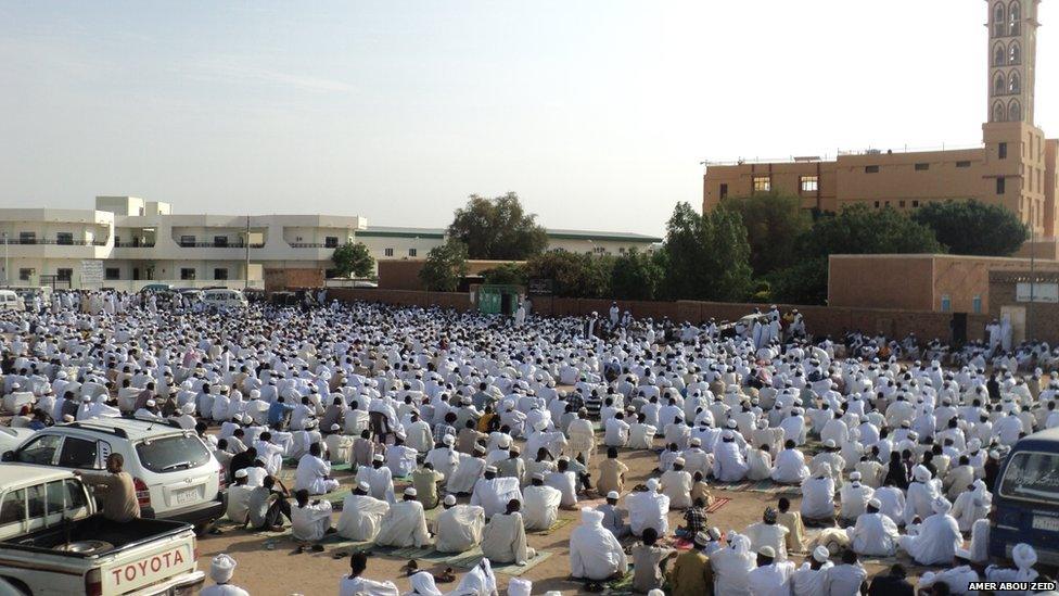 Men mostly dressed in traditional white robes sit outside mosque in Sudan during Eid prayers. Photo: Amer Abou Zeid