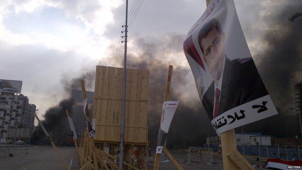 A poster of deposed Egyptian president Mohammed Morsi with plumes of black smoke during clashes between protesters and security forces in Cairo