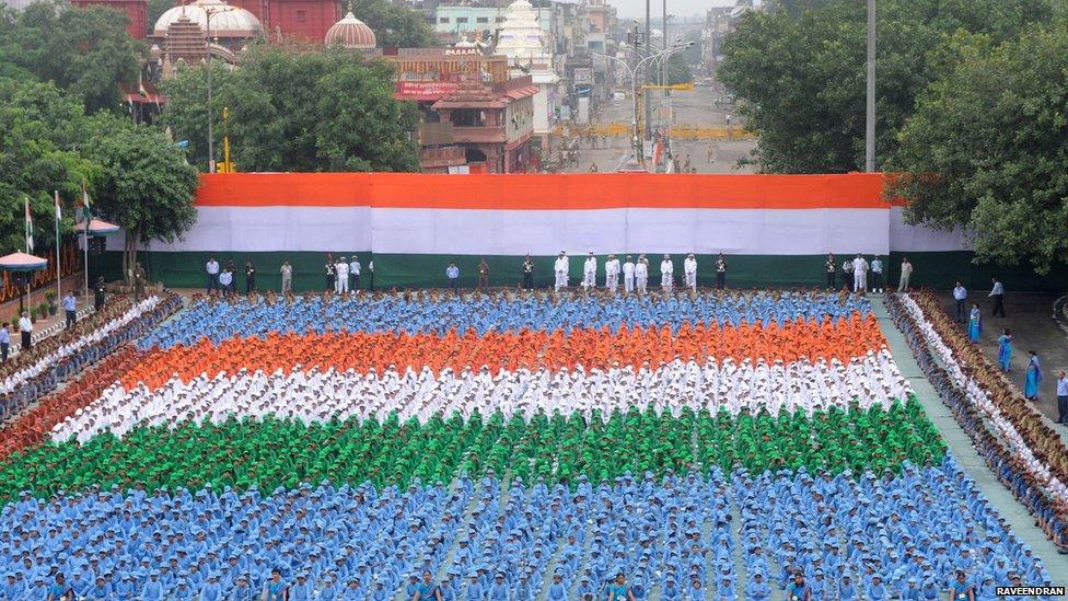Children sitting in rows beneath a flag