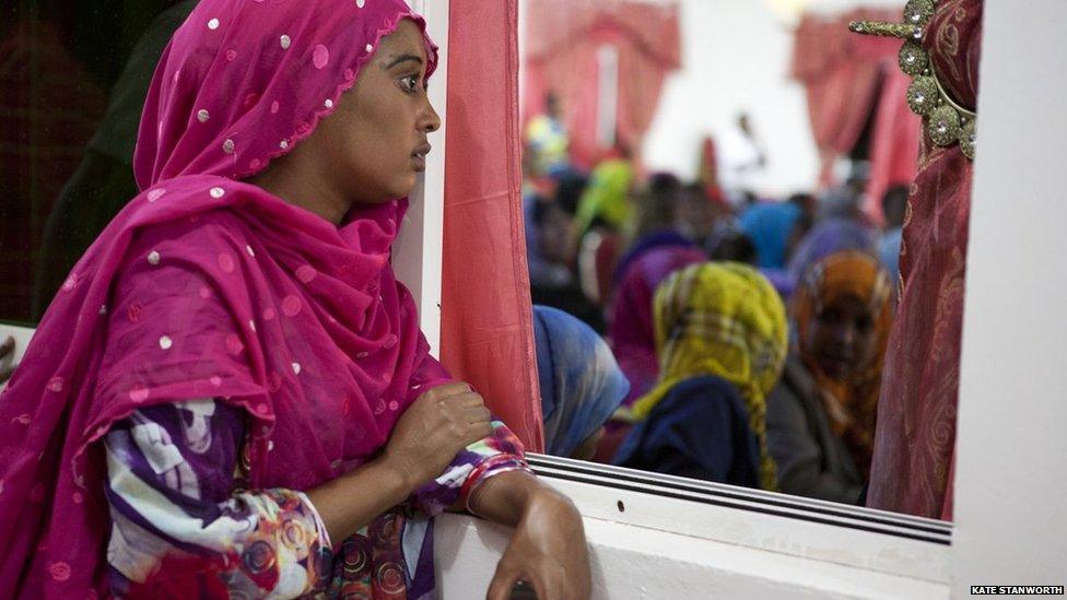 A woman watches through a window as a play is being performed, addressing the theme of corruption, during the closing ceremony of the book fair, in front of a diverse crowd of guests including government ministers and elders- Hargeisa, Somaliland