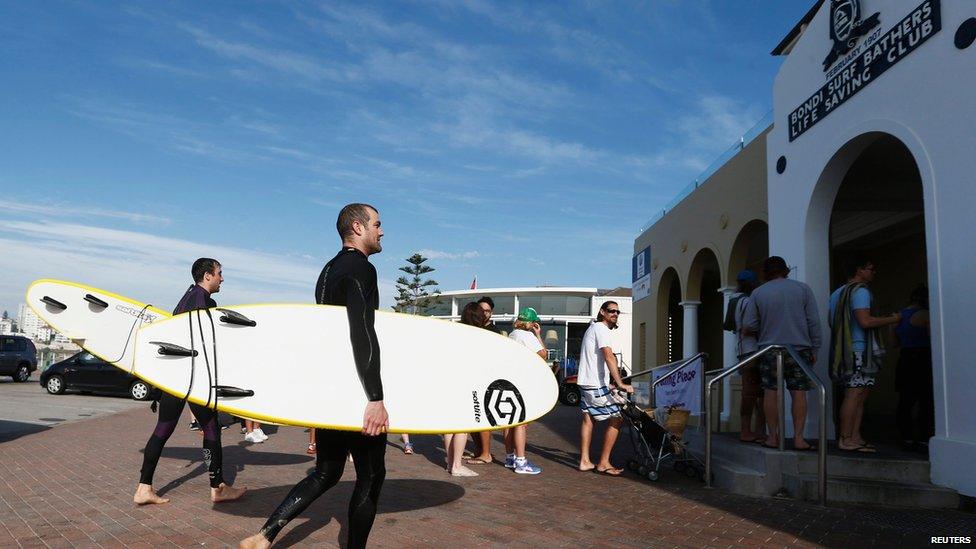 Two surfers walk past residents as they line up to vote