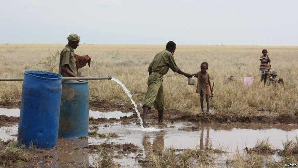 A Kenyan police reservist delivers clean water to a thirsty child at the Lotikipi Borehole