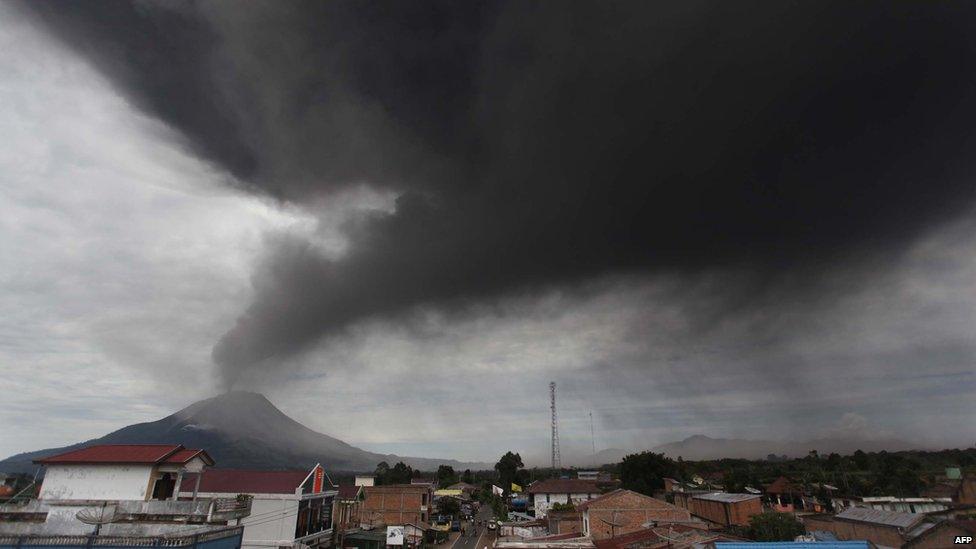 A cloud of ash rises from the crater of the Mount Sinabung volcano (back L) during a fresh eruption on 17 September, 2013, as seen from Karo district.