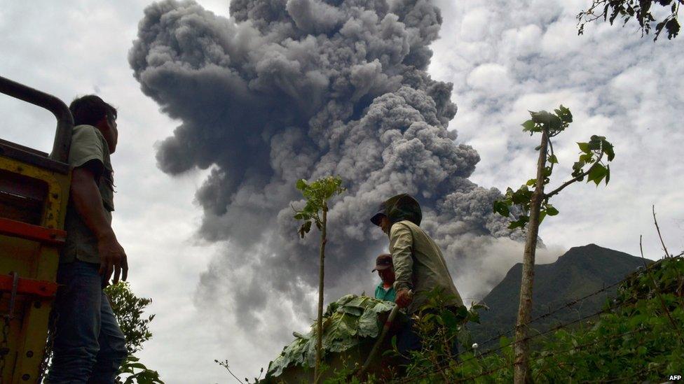 Indonesian farmers rush to harvest crops in the district of Karo as an ash cloud rises during a fresh eruption of the Mount Sinabung volcano on 17 September, 2013.