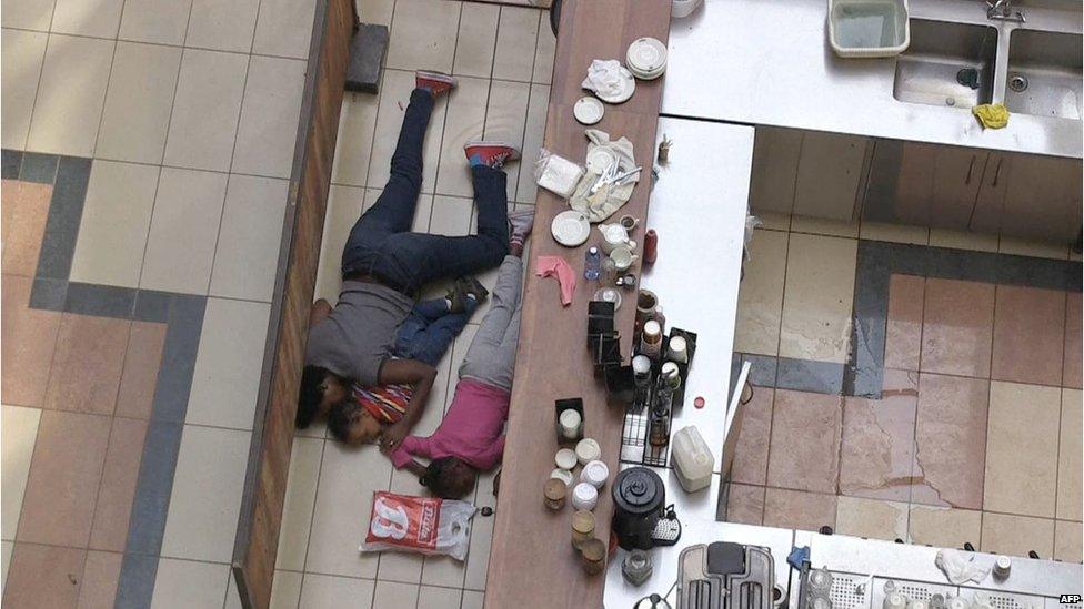 A woman and two children take cover behind a bar inside a shopping mall following an attack by masked gunmen in Nairobi (21 September 2013)