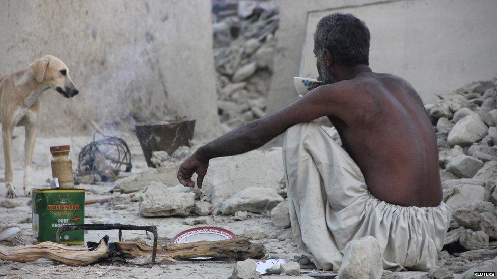 A survivor of an earthquake sits as he takes tea on rubble of a mud house after it collapsed following the quake in the town of Awaran