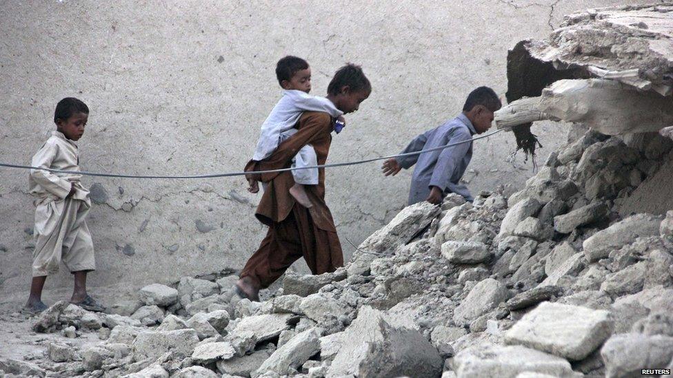 Survivors of an earthquake walk on rubble of a mud house after it collapsed following the quake in the town of Awaran