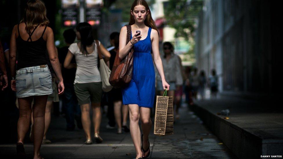 An off-duty model walks along the road studying her mobile phone.