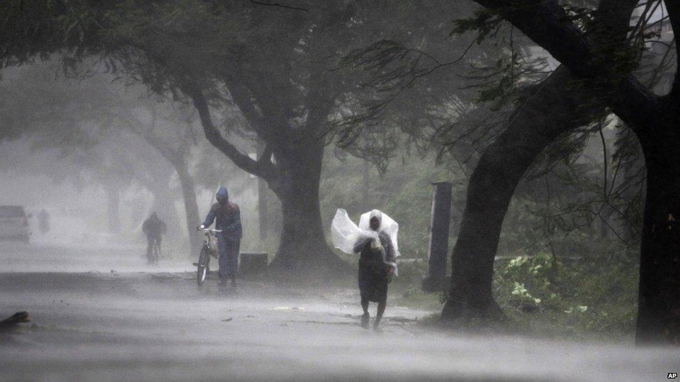 A man covers himself with a plastic sheet as a shield from the rain as he walks to a safer place near Gopalpur junction in Ganjam district