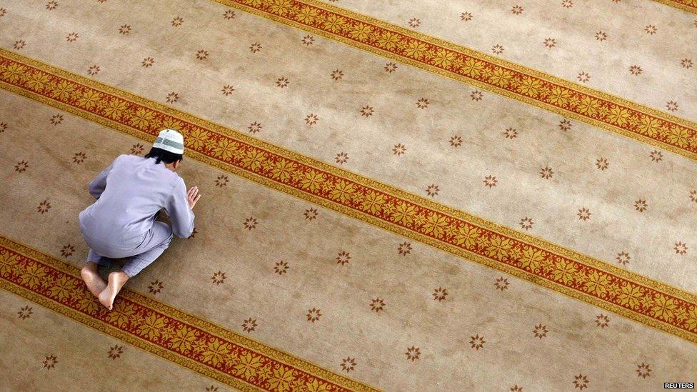 Man praying on colourful rug in a mosque in Singapore.