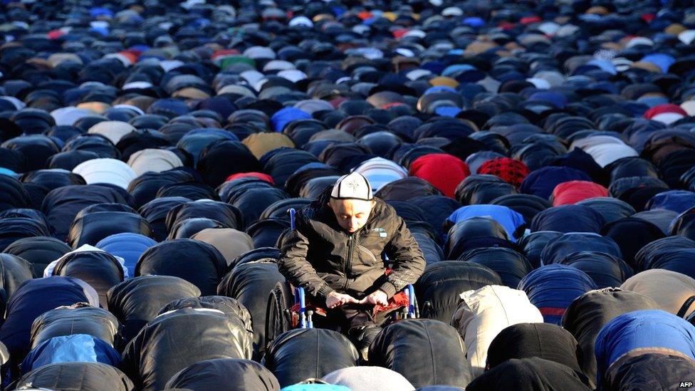 Man in wheelchair among hundreds of men kneeling in prayer at a mosque in Moscow.