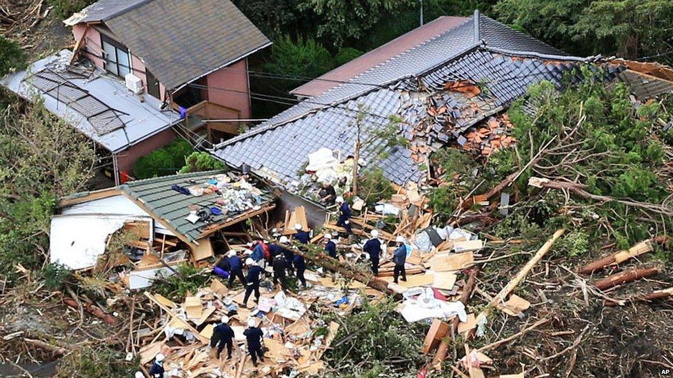Rescue workers look for survivors as they stand on the rubble of a house buried by mudslides after a powerful typhoon hit Izu Oshima island on 16 October 2013