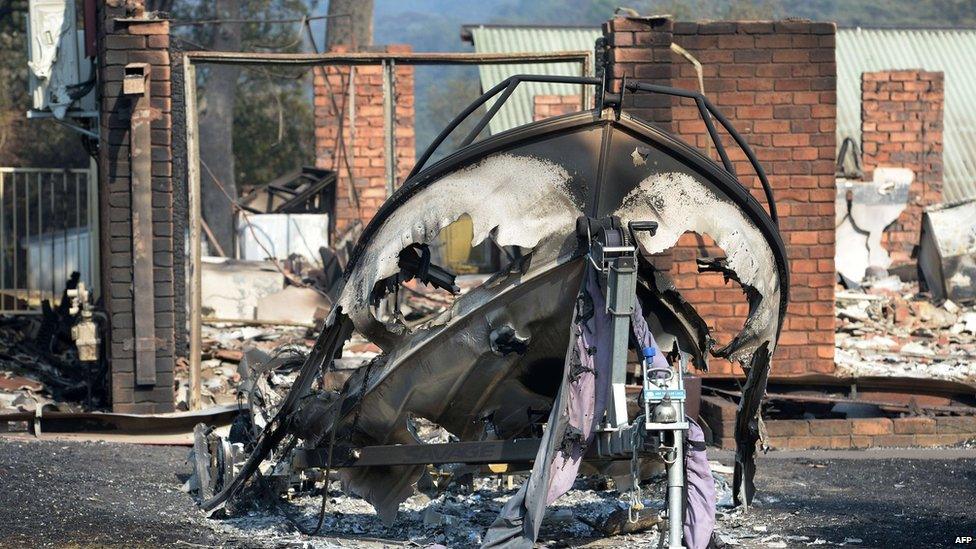 A burnt-out boat (C) sits in front of a house destroyed by bushfires in Winmalee in Sydney's Blue Mountains on 18 October 2013