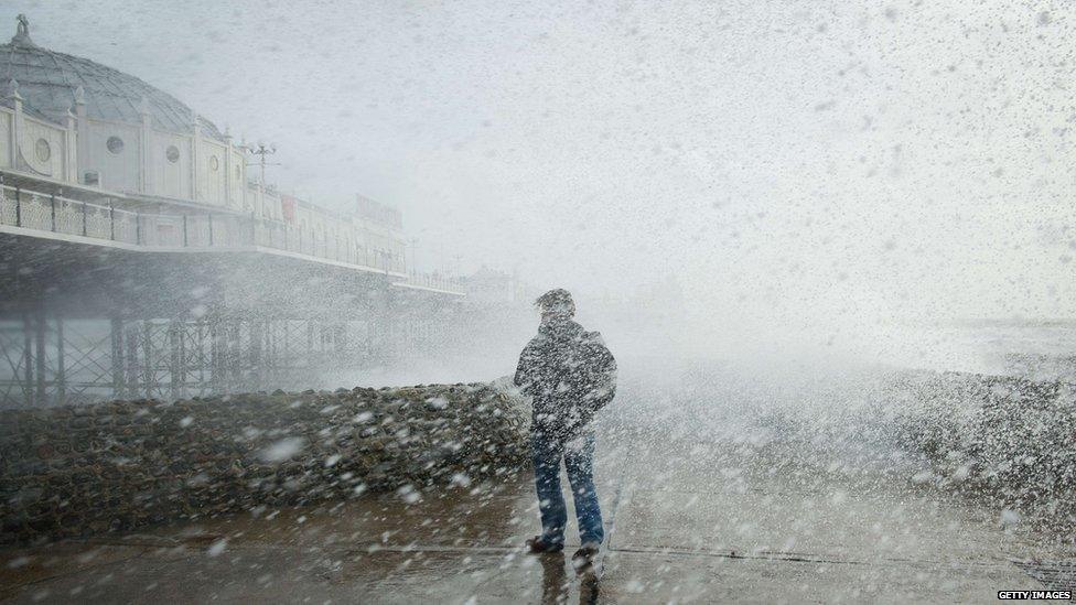 A man is soaked as large waves crash against the walls of Brighton seafront, in southern England