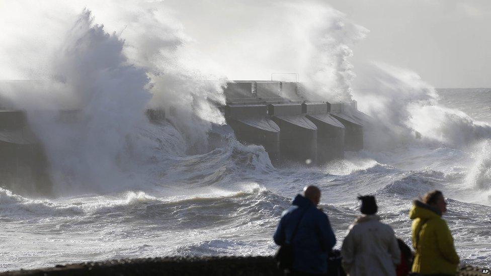 People watch the waves batter into the sea wall of a marina in Brighton,