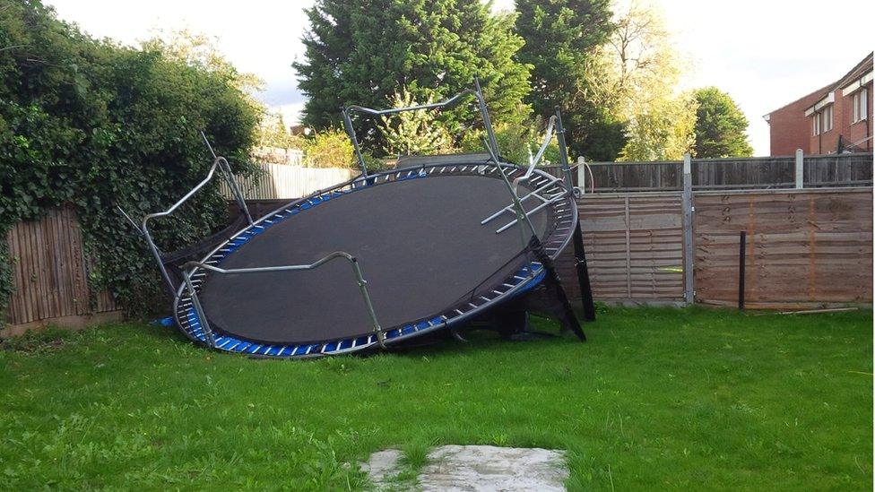 A large round trampoline lies upside down against a garden fence.