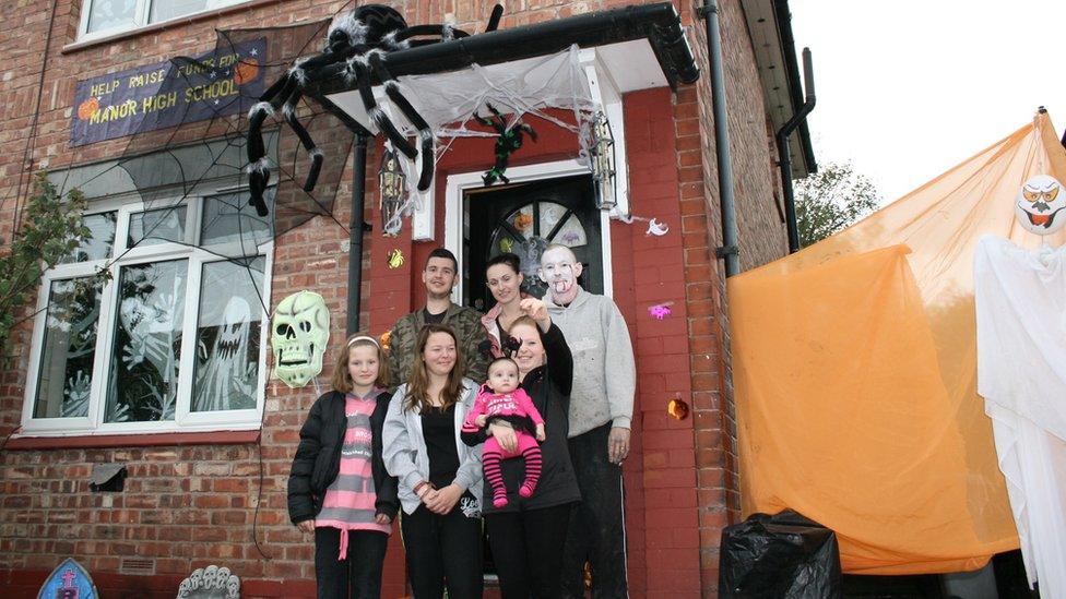 A family standing outside their home decorated for Halloween with ghosts and spiders.
