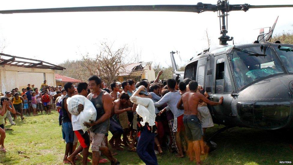 A man smiles as he carries a sack of relief goods while others rush for their share during a relief distribution in Iloilo province, central Philippines, on 11 November 2013