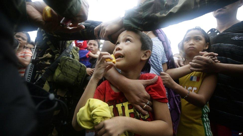 A Philippine air force officer hands out orange slices to typhoon survivors as they line up to board a C-130 military transport plane in Tacloban city, central Philippines