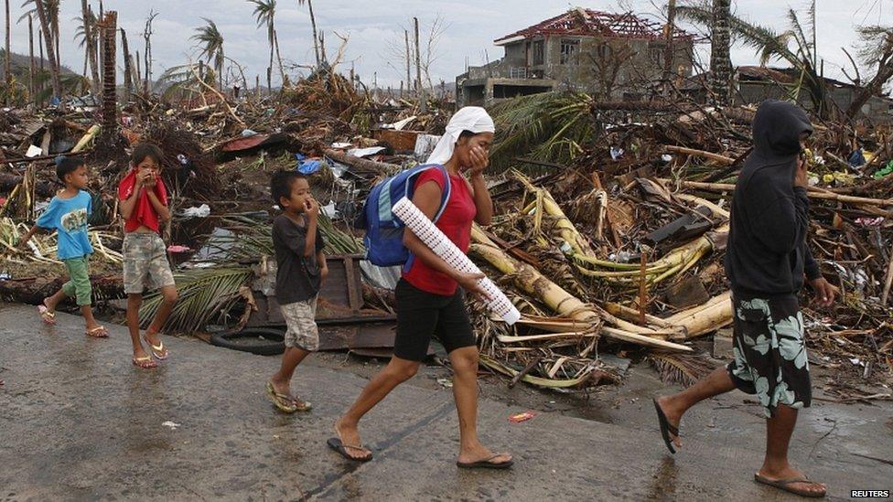 Residents cover their noses as they walk past debris with stench of corpses along a road in Palo town, in Leyte province in central Philippines