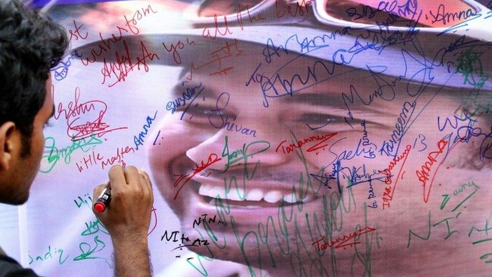 A fan of Sachin Tendulkar writes a message on a poster displayed in Bangalore on 13 November 2013