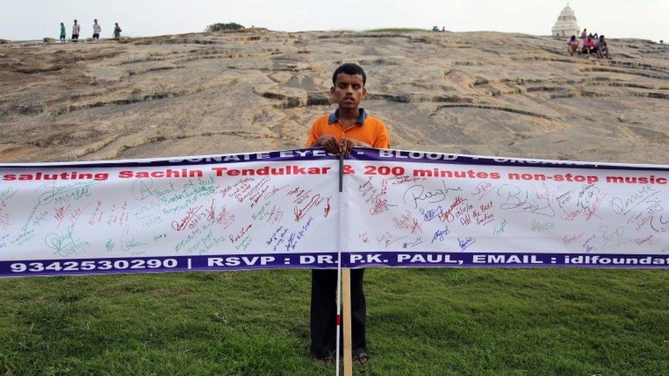 A member of a non-governmental organisation for the blind holds banners with messages for Sachin Tendulkar in Bangalore on 13 November 2013