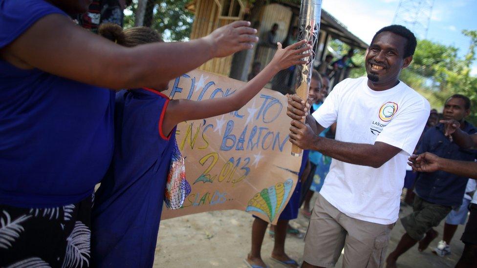 A batonbearer carries the Queen's Baton past local children who made handmade signs to welcome its arrival in Honiara, Solomon Islands.