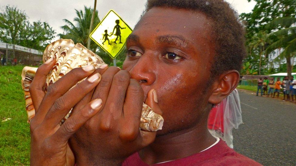 A man plays a sea shell to welcome the baton to the New Ireland province