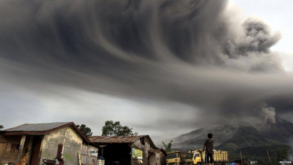 A woman looks on as Mount Sinabung spews ash, as pictured from Sibintun village in Karo district, Indonesia's north Sumatra province, 18 November 2013