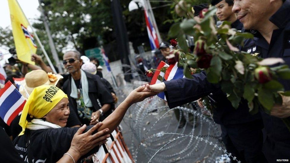 An anti-government protester touches the hand of a policemen across barbed wire after giving him flowers at a barricade near a government building chosen as a protest site in Bangkok, 25 November 2013