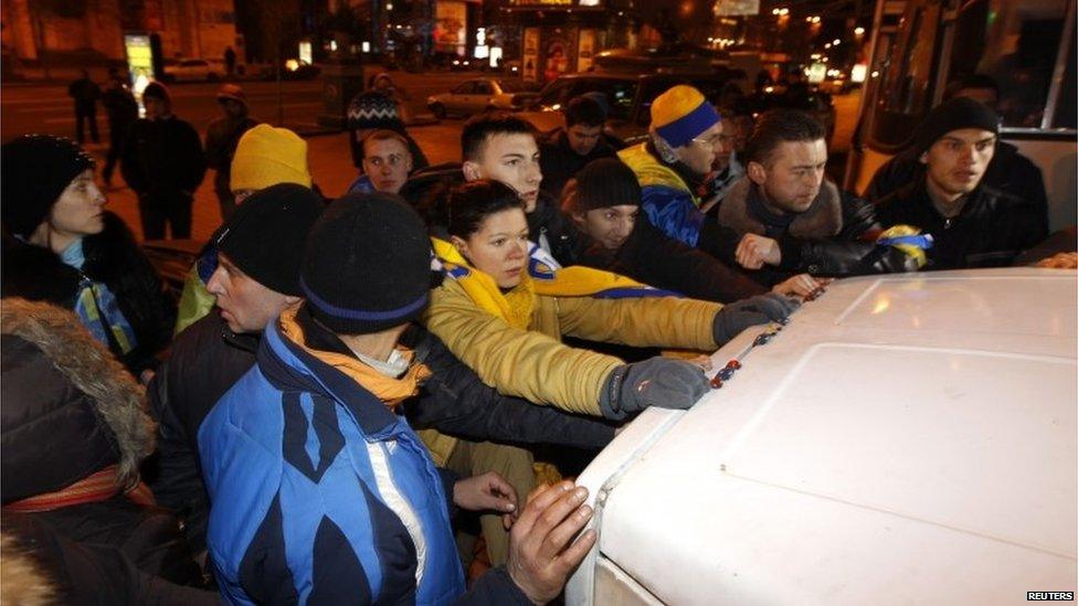Protesters block a police car holding detained people